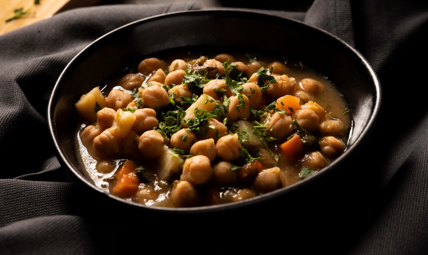 A bowl of chickpea and spinach curry , surrounded by fresh cilantro, lime wedges, and spinach leaves.