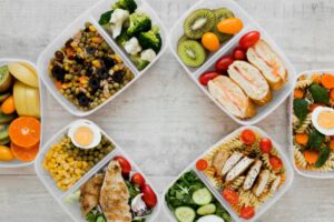 A variety of healthy meal prep containers filled with fruits, vegetables, proteins, and grains, arranged on a light wooden surface.