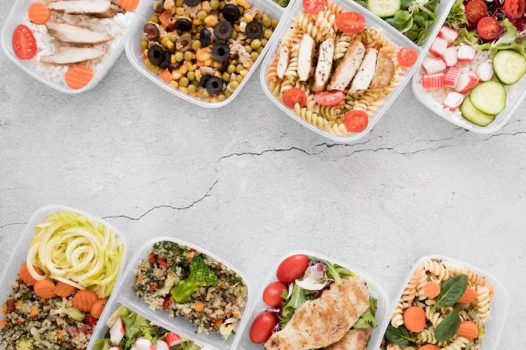 A variety of healthy meal prep bowls featuring chicken, pasta, salads, grains, and vegetables on a light grey surface.chicken, pasta, salads, grains, and vegetables on a light grey surface.