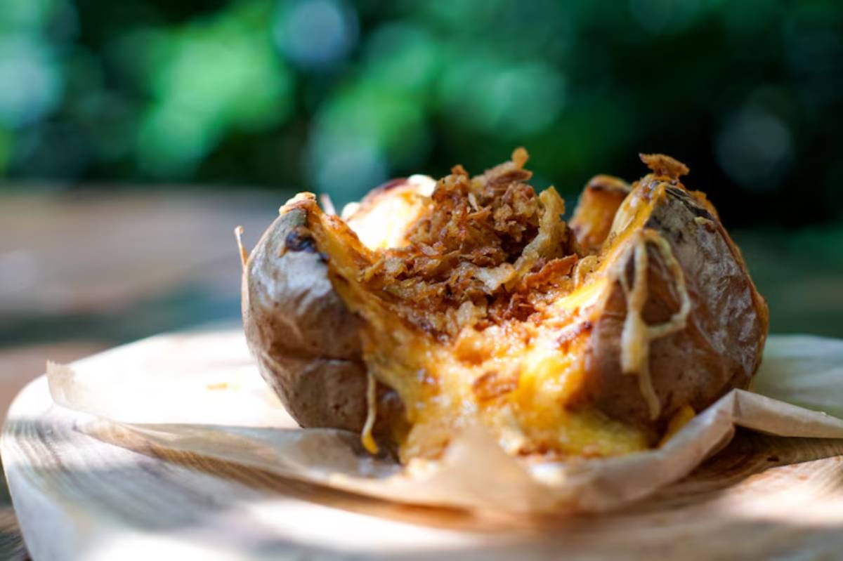 A baked potato topped with melted cheese and crispy onions, oozing deliciousness, presented on a wooden surface.