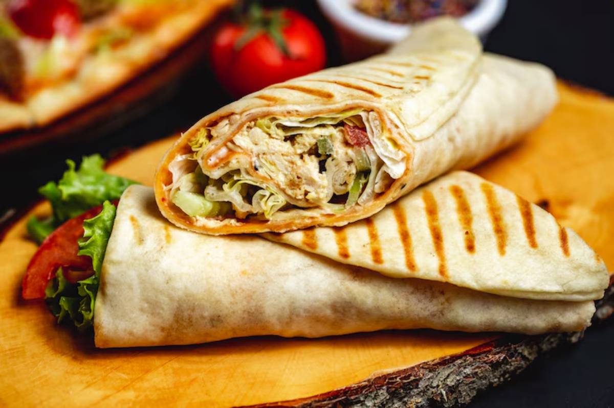 A grilled tortilla wrap filled with shredded chicken, fresh lettuce, and tomatoes, served on a wooden board.
