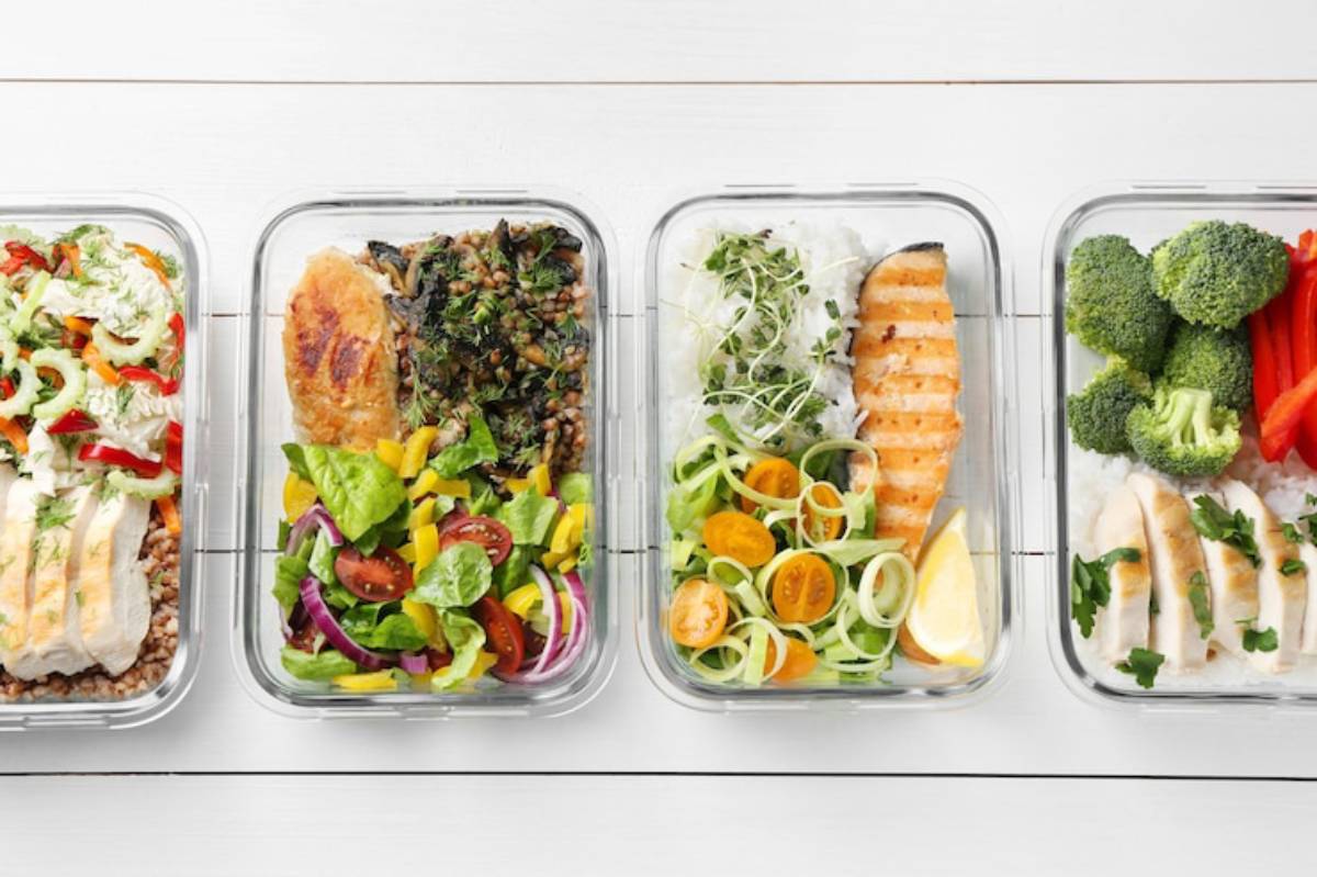 Four meal prep containers filled with colorful, healthy meals: salads, grilled fish, vegetables, and grains on a white background.