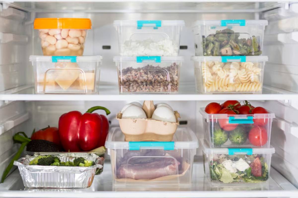 A well-organized fridge displays various containers of leftovers, fresh vegetables, eggs, and salad ingredients on clear shelves.
