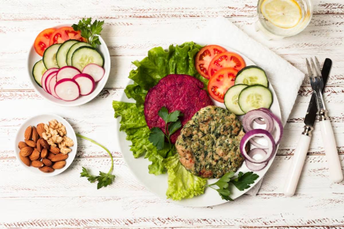 A vibrant plate featuring a green lettuce bed, beet and veggie patties, fresh tomatoes, cucumbers, onions, and bowls of nuts and radishes.