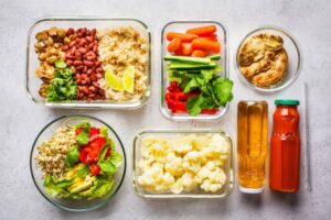 A variety of meal prep containers filled with beans, grains, vegetables, and sauces, showcasing healthy, colorful food options.