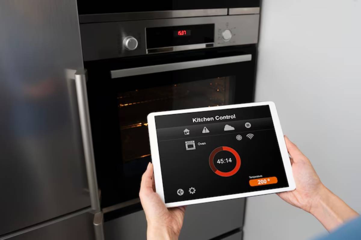 A person holding a tablet displaying kitchen control settings for an oven, with a timer and temperature of 200°C visible.