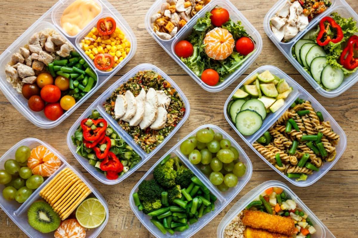 A colorful assortment of meal prep containers filled with chicken, vegetables, fruits, and grains on a wooden surface.