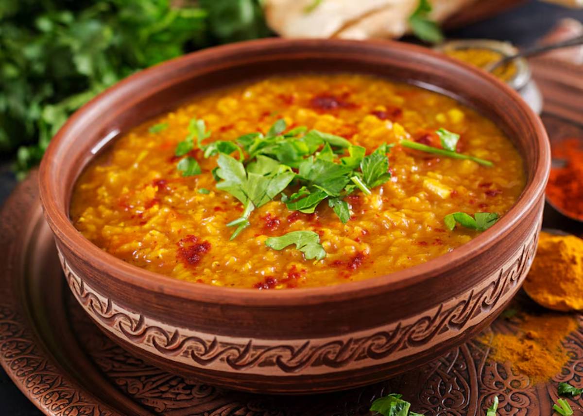 A bowl of yellow lentil soup garnished with fresh coriander, served on a decorative plate with spices in the background.