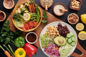A vibrant assortment of fresh vegetables, legumes, and nuts arranged artistically on a wooden board, with lemon slices and spices.