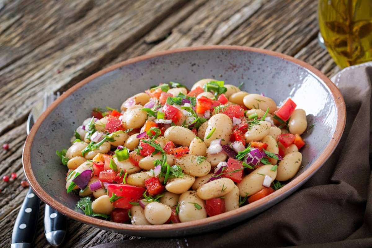 A bowl of white bean salad mixed with diced tomatoes, onions, and fresh herbs, set on a rustic wooden table.