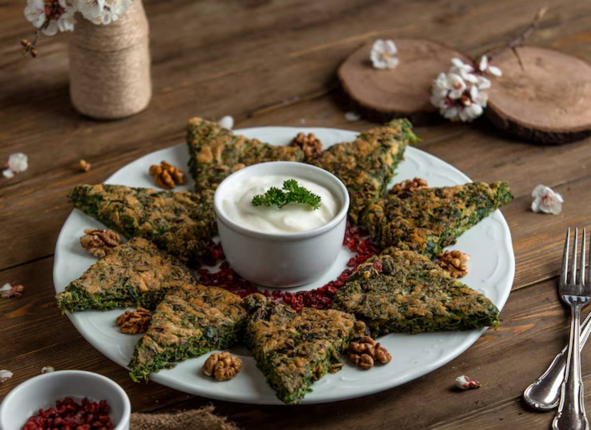 A circular plate displays triangular green pastries arranged around a bowl of yogurt, garnished with parsley and scattered nuts.
