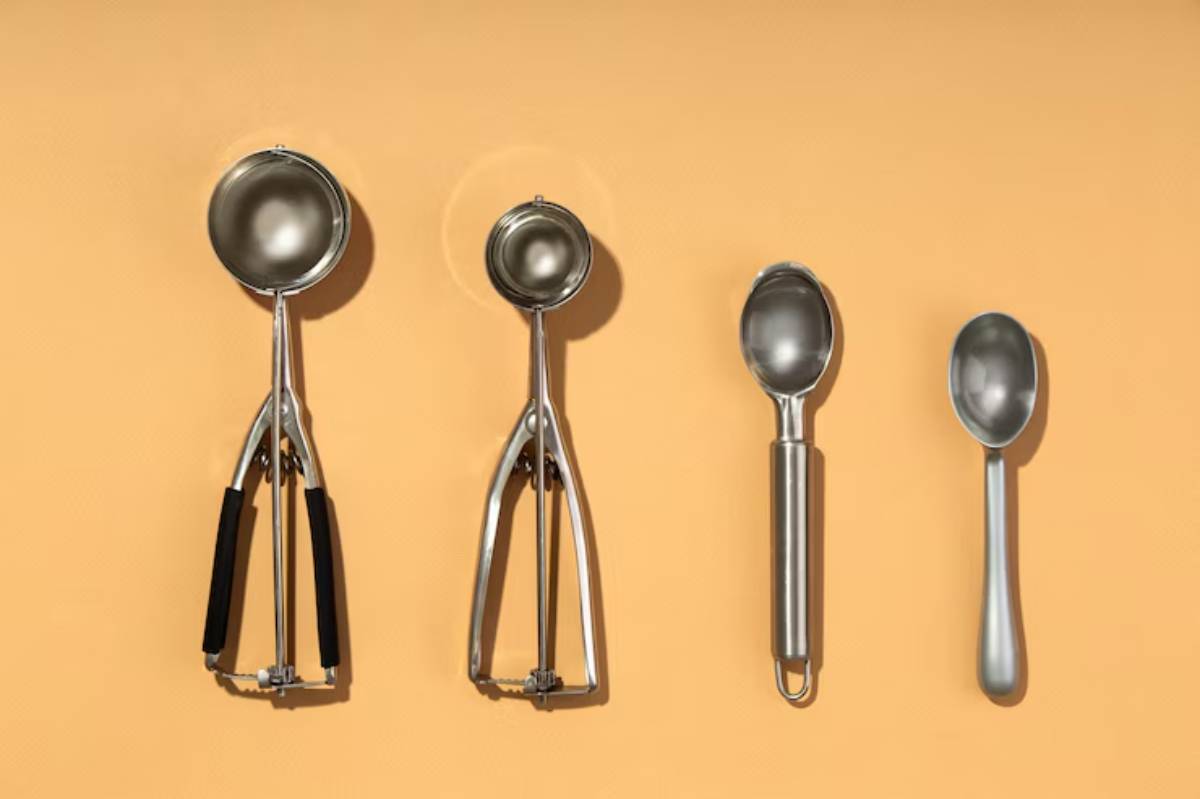 Four metal scoops in varying sizes, arranged horizontally on a bright orange background, showcasing their sleek designs.