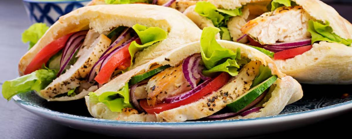 A close-up of pita pockets stuffed with grilled chicken, lettuce, tomato, onions, and cucumbers on a decorative plate.