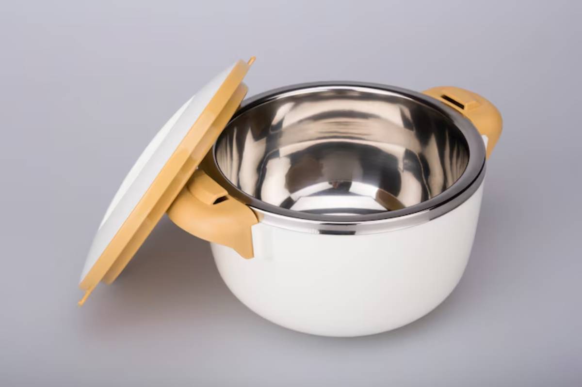 A white cooking pot with a stainless steel interior and a light yellow lid, slightly ajar, showcasing its shiny interior.