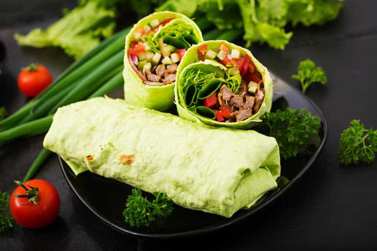 Two colorful lettuce wraps filled with vegetables and beef, served on a black plate with fresh tomatoes and green onions.