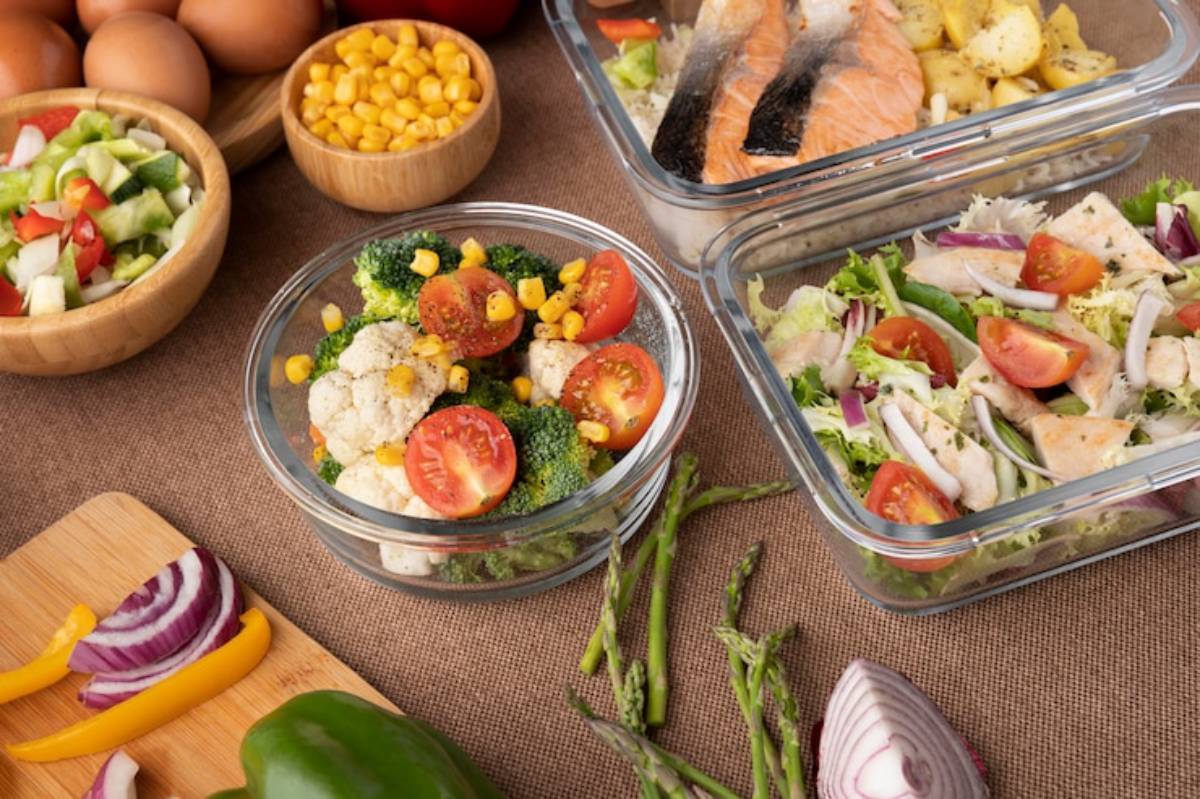 A variety of healthy meal prep dishes featuring colorful vegetables, salmon, chicken salad, and fresh ingredients on a rustic table setting.