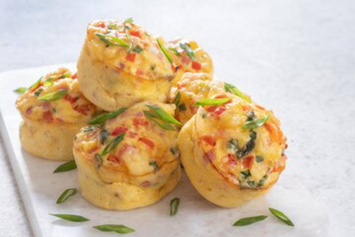 A plate of golden, fluffy egg muffins filled with vegetables and topped with green onions, showcasing a delicious, savory breakfast option.